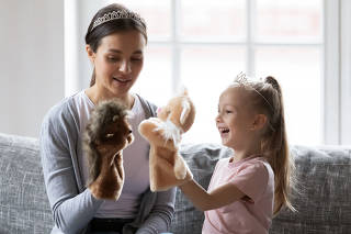 Happy little girl wearing crown playing hand toys with babysitter.