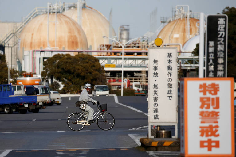 homem de bicicleta pedala em pátio de refinaria com letreiros em japonês