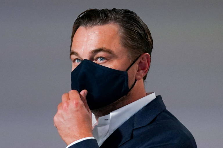 DiCaprio, com máscara preta, coloca a mão próximo à boca e olha para frente