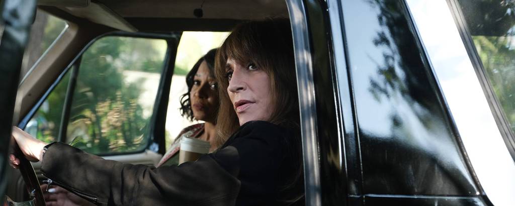 Duas mulheres sentadas dentro de um carro preto olhando para fora