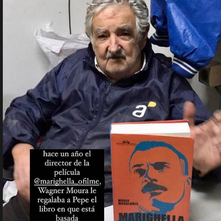 um senhor idoso de cabelos e bigode grisalhos está sentado e à sua frente está o livro Marighella