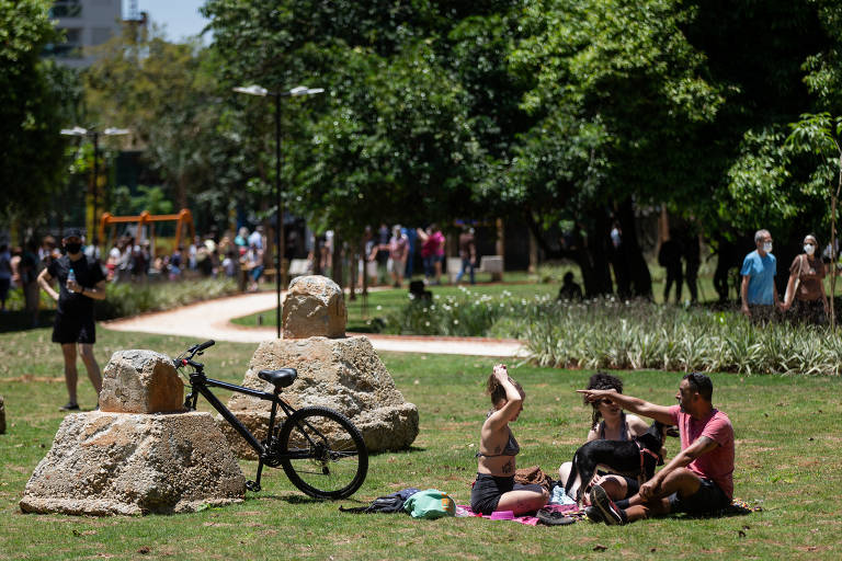 Pessoas sentadas em parque, próximo a uma bicicleta apoiada em pedra