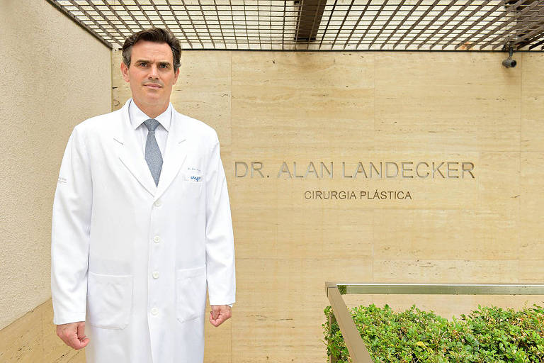 O cirurgião plástico Alan Landecker de jaleco branco, em pé, na frente de seu consultório 
