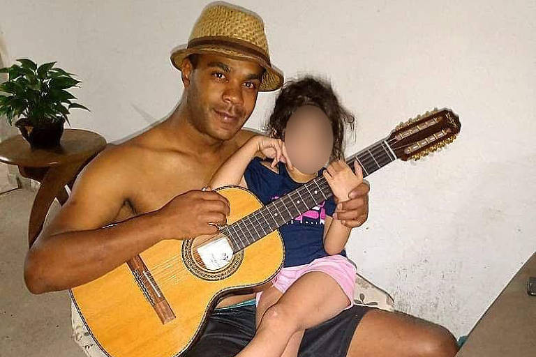 A imagem mostra Anderson, que é um homem negro, sentado segurando um violão e com sua filha, uma menina branca, no colo
