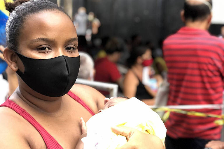 mulher com máscara segura bebê em fila em Salvador