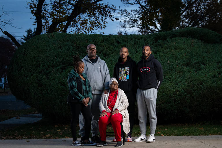 Quatro membros de uma família posam para foto, em pé, ao lado de uma pessoa sentada