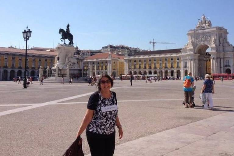 Telma é uma mulher idosa, com cabelo curto e castanho; ela posa para foto em frente a um ponto turístico de Portugal