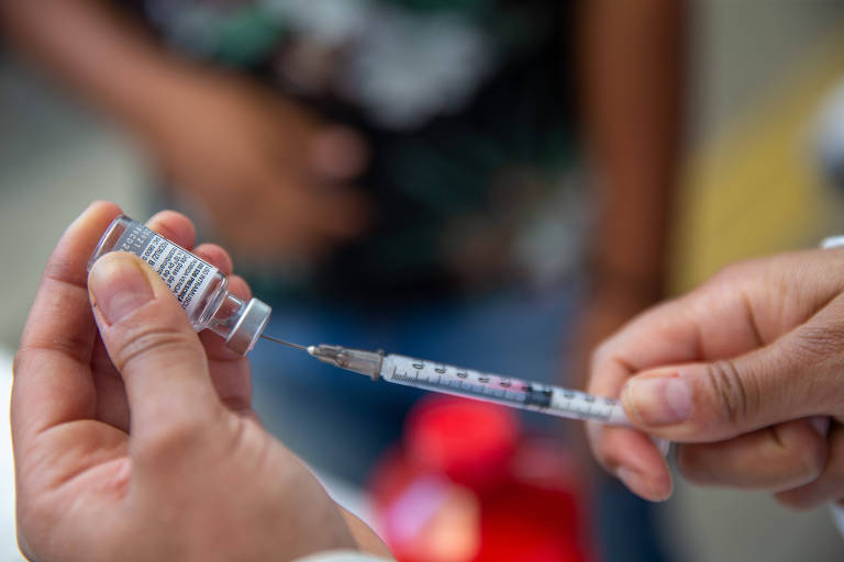 Mãos seguram frasco de vacina e seringa com agulha