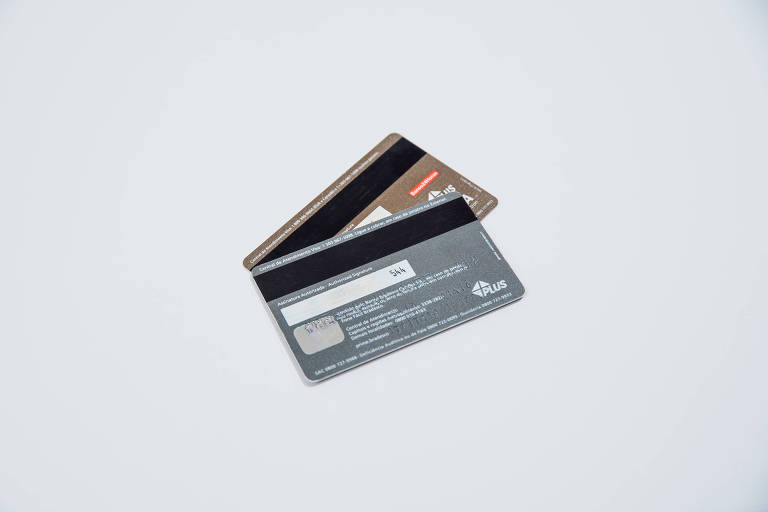 Sobre um fundo branco, dois cartões de crédito, sobrepostos, um dourado e em cima, um cinza