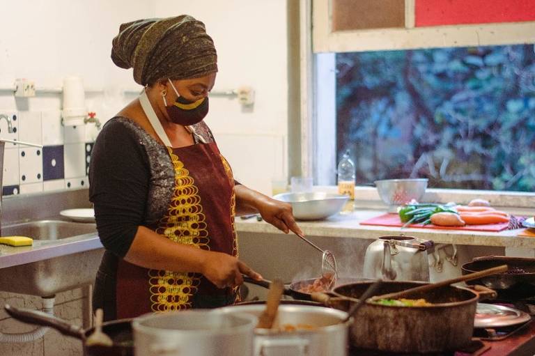 Uma mulher com máscara e turbante cozinhando
