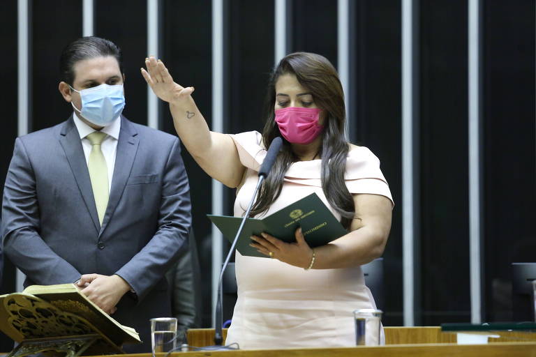 Mulher com máscara rosa segura livro e presta juramento na mesa da Câmara dos Deputados
