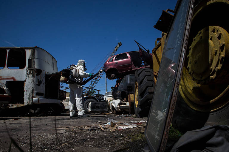Funcionário aplica inseticida em terreno municipal que serve de depósito para carcaças de carros abandonados