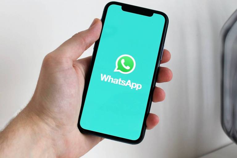 Foto mostra celular com tela verde e logo e nome do WhatsApp sendo segurado por uma mão