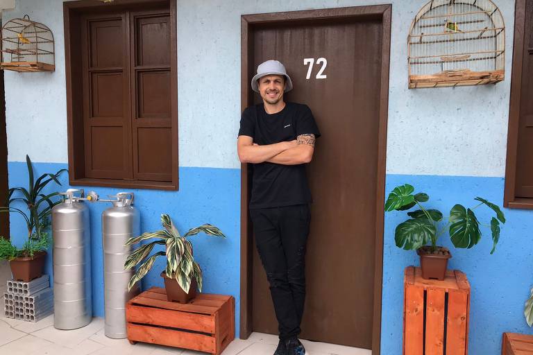 Homem parado em frente a porta marrom com número 72 entre paredes azuis