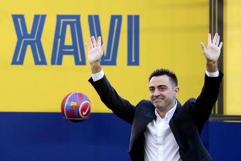Xavi, com paletó e camisa branca, apresentado no Barcelona; um banner atrás dele tem seu nome em amarelo e azul