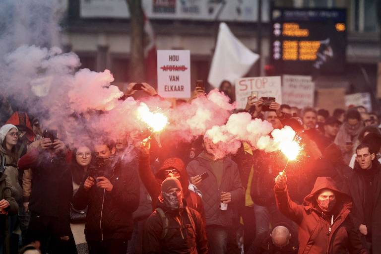 Fileira de pessoas com máscaras, segurando cartazes e segurando sinalizadores acesos, que emitem luz e fumaça vermelha