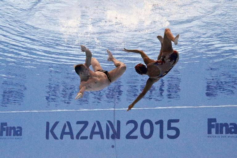Os dois se movimentam embaixo da água; na parede está escrito Kazan 2015, local e sede do Mundial