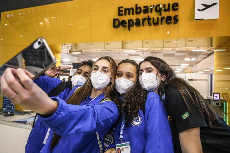 Quatro atletas com máscara tiram selfie no aeroporto, em frente ao embarque