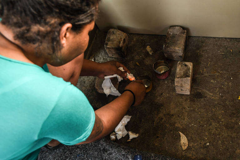 Mulher de 33 anos está agachada e mostra o 'fogão' que faz com latas, tijolos e álcool