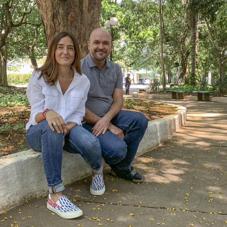 casal de homem e mulher está sentada em beira de calçada de praça bem arborizada