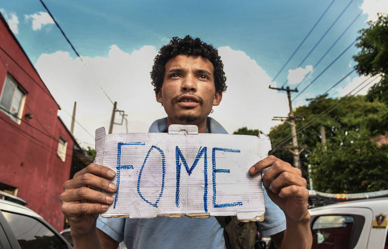 Jovem negro segura folha escrito 'fome' em meio ao trânsito em São Paulo 