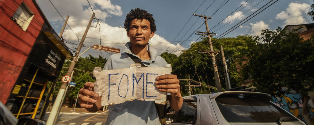 Jovem negro segura cartaz escrito fome em cruzamento