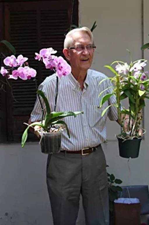 O frei Cláudio van Balen com vasos de flores nas mãos.