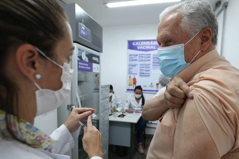 Enfermeira segura seringa enquanto idoso puxa para cima a manga da camisa, para receber a vacina