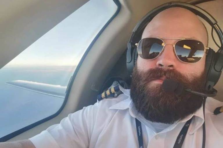 Homem de barba e óculos escuro posa para foto dentro de uma aeronave