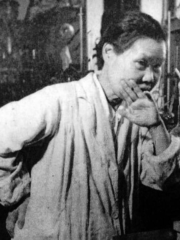 Imagem em preto e branco mostra uma pessoa com uma mão na cintura e a outra próxima a boca