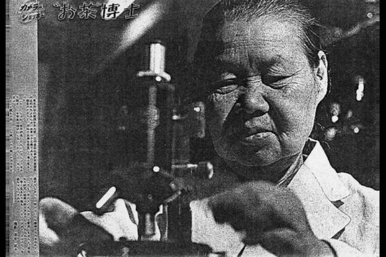 Imagem em preto e branco mostra pessoa manipulando um microscópio