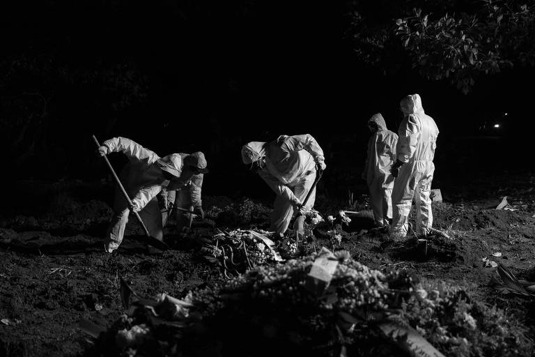Três sepultadores com trajes brancos de proteção jogam terra sobre cova; outros dois observam