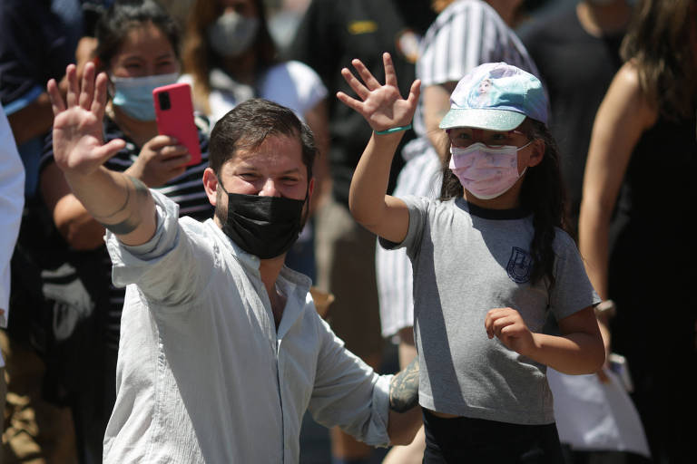 Usando máscara facial, o candidato esquerdista à Presidência, Gabriel Boric, acena para apoiadores em Santiago do Chile; ao seu lado, uma menina, também de máscara, acena igualmente