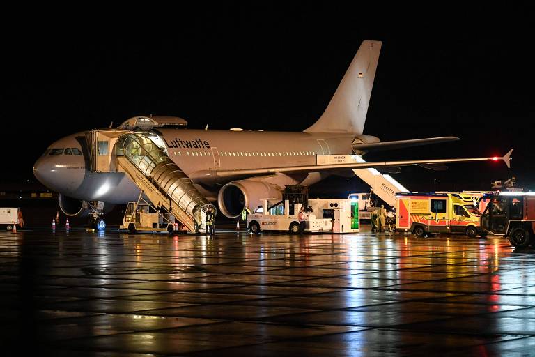 Avião à noite em pista de aeroporto, com escadas nas portas da frente e de trás e ambulâncias na pista