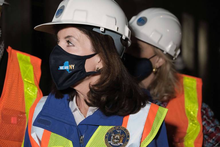 Foto mostra a governadora do estado de Nova York, Kathy Hochul paramentada com equipamentos de proteção enquanto visita uma obra 