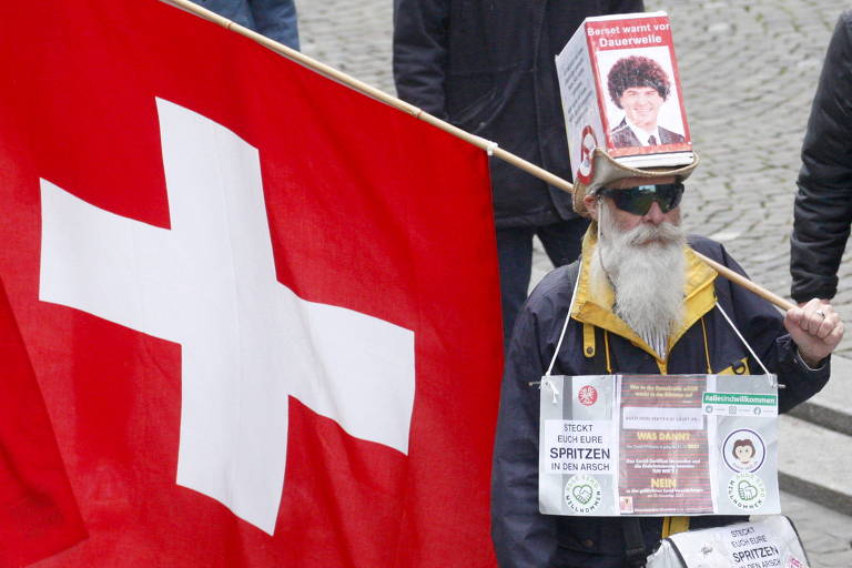 Homem de barba branca e óculos escuros segura bandeira da Suíça, vermelha com uma cruz branca
