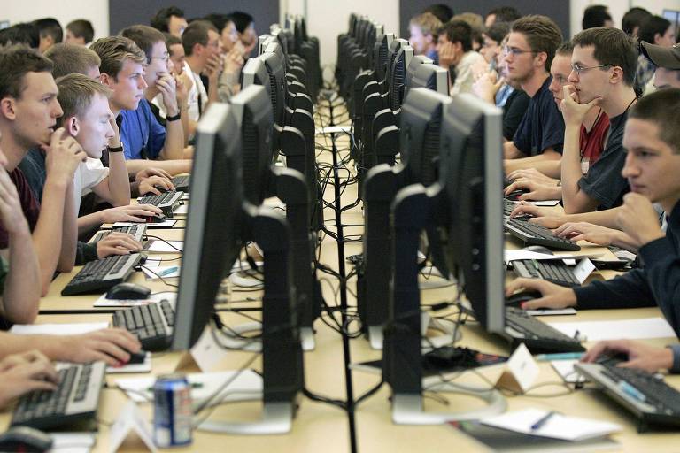 Inúmeras pessoas sentadas em frente a computador colocados uns ao lado dos outros