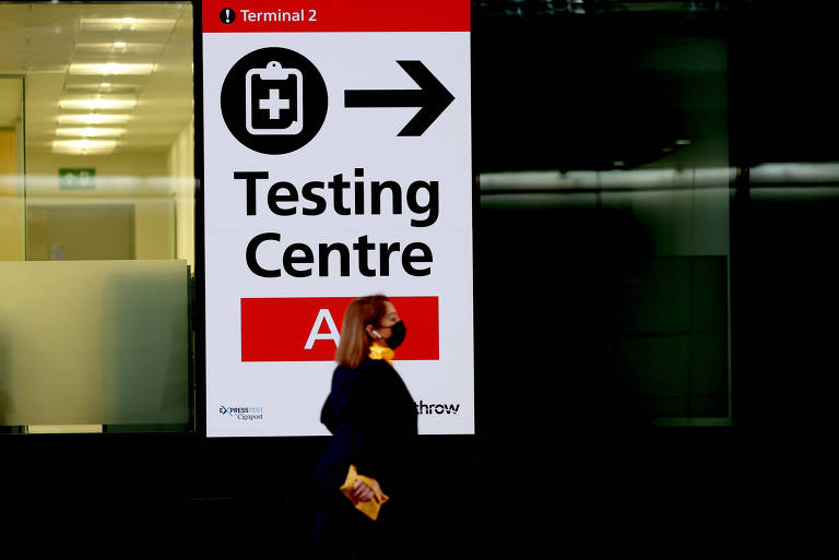 Uma mulher passa em frente de uma placa indicando o centro de testagem de Covid-19 em um aeroporto do Reino Unido.