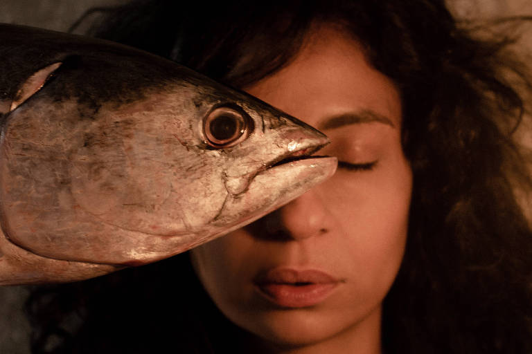 Uma mulher com um olhe fechado e um peixe cobrindo metade de seu rosto