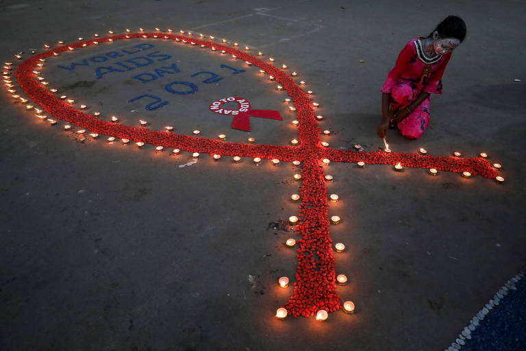 Menina agachada ao lado de laço vermelho, símbolo do HIV, desenhado no chão e cercado de velas
