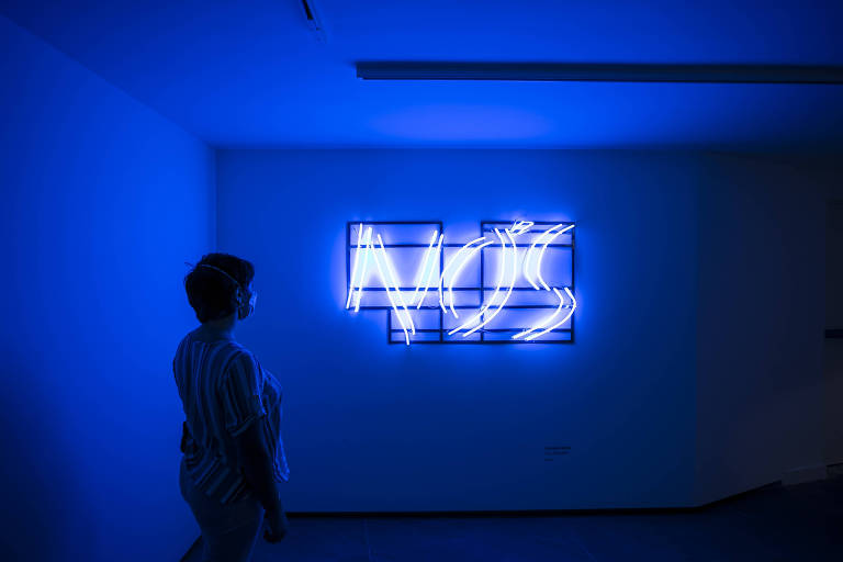 Mulher observa néon azul com a palavra "nós"