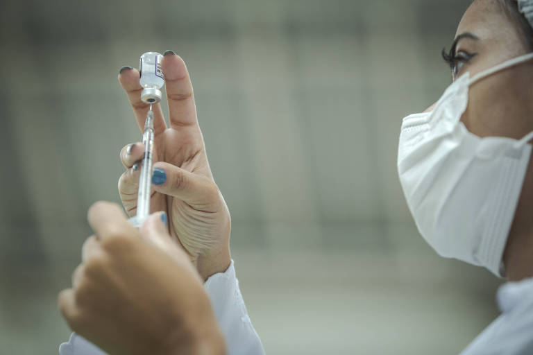 Profissional de saúde enfia uma agulha no frasco com vacina contra a Covid