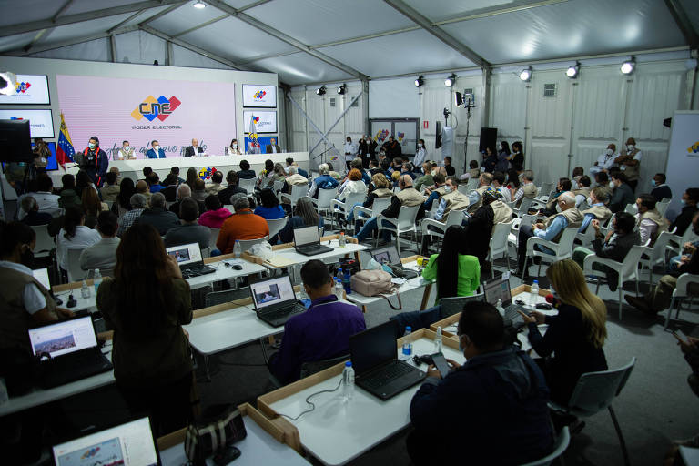 Em uma sala grande, com mesas cheias de notebooks, observadores internacionais e jornalistas acompanham em Caracas a divulgação de resultados das eleições regionais na Venezuela