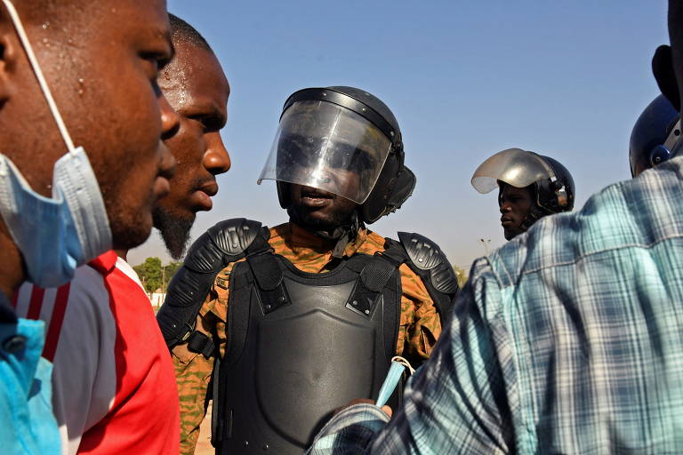 Policial ao lado de manifestantes da Burkina Fasso que, durante a pandemia, organizaram protesto pedindo a renúncia do presidente Roch Marc Christian Kaboré e a saída das tropas francesas que patrulham o país