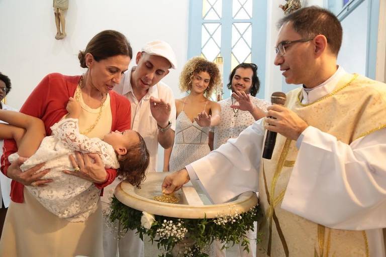 Flora Gil e o música Pedro Baby (à dir.) batizam Sol de Maria, neta de Preta Gil, sendo observados pelos pais da menina, Laura Fernandez e Francisco Gil (ao fundo)