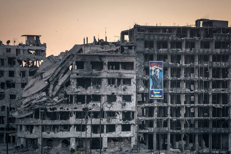 Cartaz com a imagem do ditador Bashar al-Assad pendurado em prédio em ruínas na cidade de Homs, na Síria