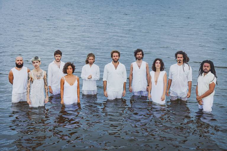 Os dez integrantes do grupo Foli Griô Orquestra posam vestidos de branco para a câmera, envoltos por água até a cintura