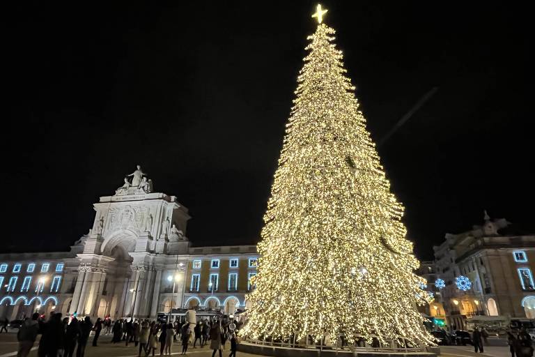 Grande árvore de Natal iluminada se destaca em frente ao brando da fachada dos prédios e do Arco da Rua Augusta, em Lisboa