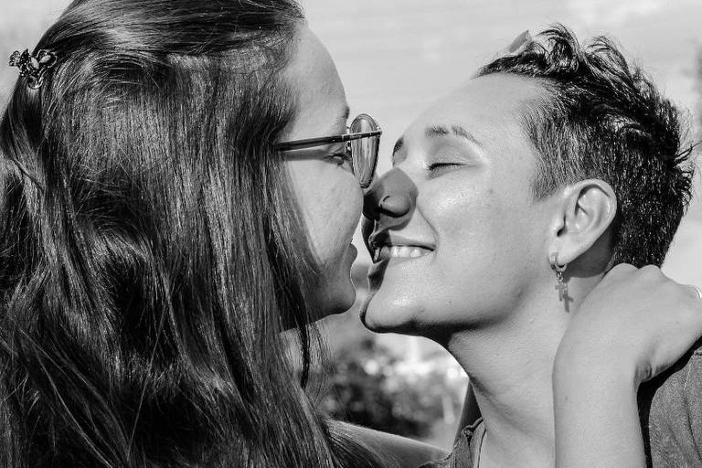 foto preto e branco de beijo na boca de duas mulheres, uma de cabelo comprido e óculos e outro de cabelo curto