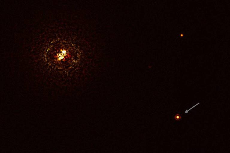 Uma mancha luminosa à esquerda e dois pontos brilhantes à direita; o ponto brilhante à direita e abaixo tem uma seta, indicando ser o planeta b Centauri b. A mancha à esquerda é a posição da estrela dupla b Centauri.
